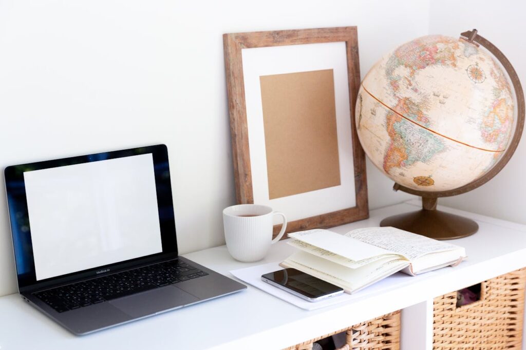 Laptop with empty screen placed near smartphone and organizer with blank frame and retro glove aside during coffee break in room